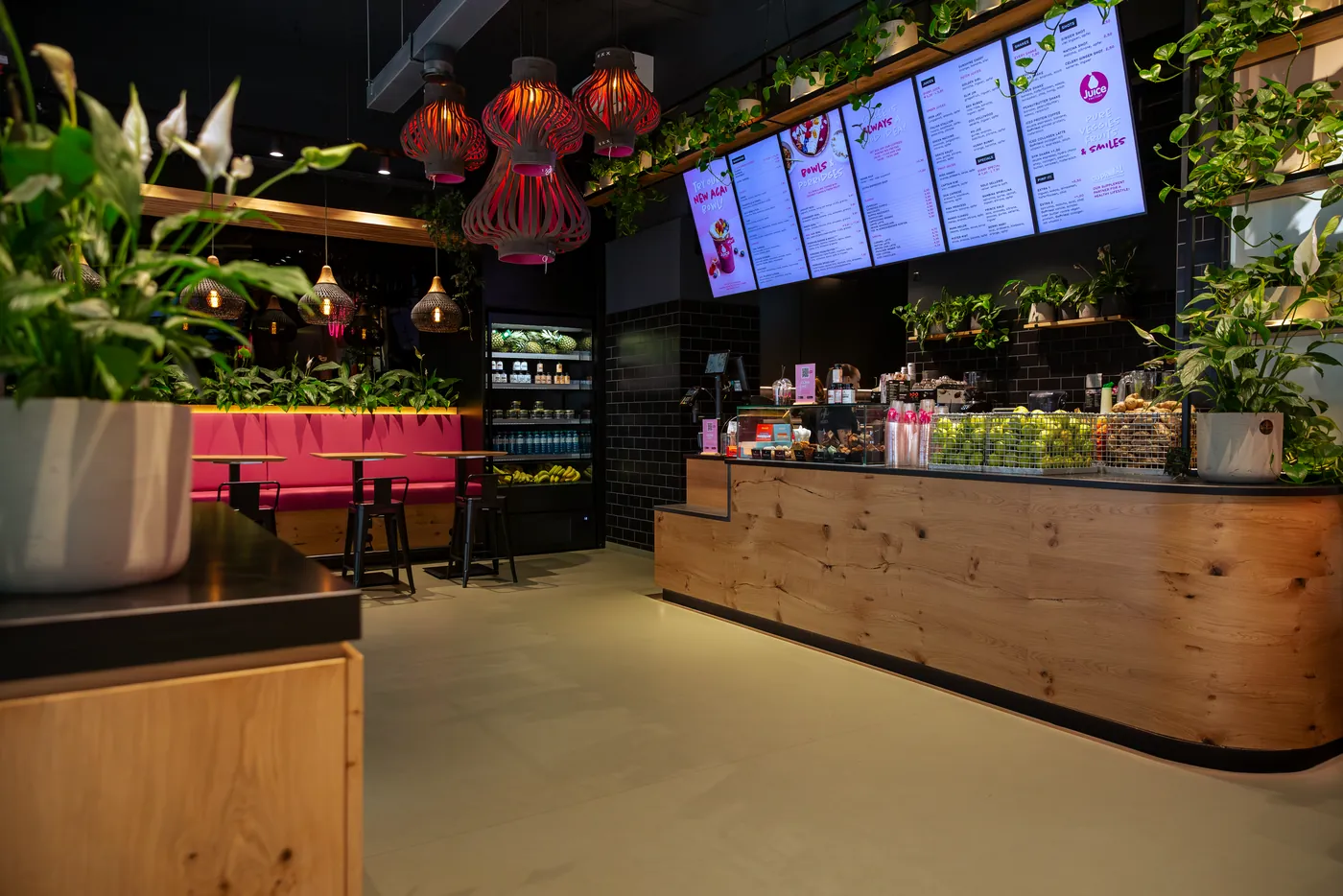 Juice Factory on Währinger Straße: wooden counter with fruit baskets, menu screens and plants, the pink bench behind