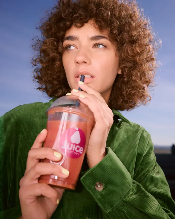 Frau mit Locken trinkt einen Juice am Flughafen Wien