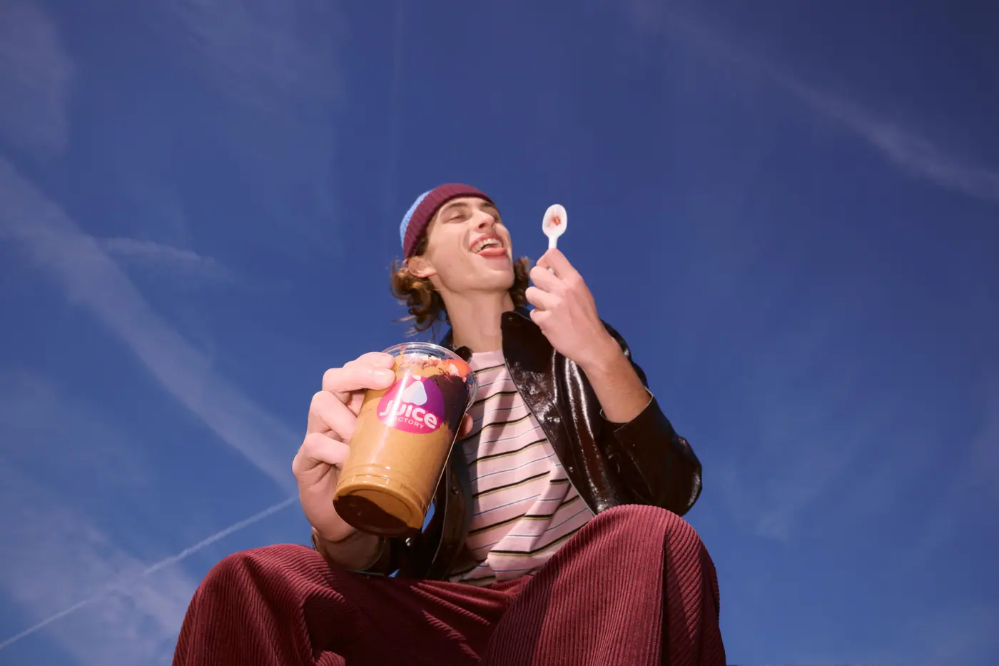 A laughing guest with an iced latte in a Juice Factory cup against a blue sky