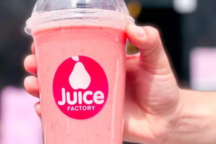 Juice-Factory-Becher vor dem pinken Logo