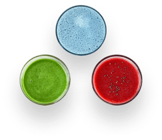 Drei Gläser Saft von oben gesehen: ein blaues, ein grünes und ein rotes mit schwarzen Samen oder Chiasamen oben drauf, angeordnet in einem dreieckigen Muster auf weißem Hintergrund.