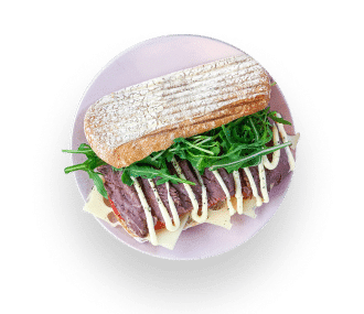Ein Sandwich auf einem runden rosa Teller, gefüllt mit Rindfleischscheiben, Käse, frischem Rucola und beträufelt mit Mayonnaise, serviert auf einem rustikalen Ciabatta-Brötchen.